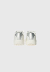 Weiße Sneaker mit silbernen metallischen Akzenten an der Ferse, Gummisohle und minimalistischer Gestaltung mit dezentem Branding auf der Rückseite.