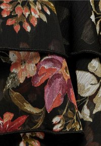 Tissu noir avec des motifs floraux superposés en rouge, violet, orange et beige, avec des feuilles et des pétales détaillés dans un matériau doux et texturé.