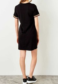 Černé krátké šaty s kontrastními barevnými pruhovanými akcenty na rukávech, jednoduchý design a rovný střih. Nositelná s černými teniskami.