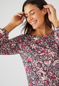 Maglietta a maniche lunghe con uno sfondo scuro e un motivo floreale colorato in rosa, rosso e blu. Tessuto morbido con scollo rotondo.