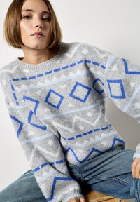 Maglione grigio a maglia con motivi geometrici blu e azzurri, dotato di scollo rotondo e maniche larghe, realizzato in un tessuto morbido e texturizzato.