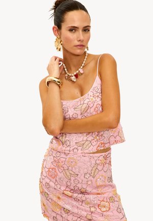 Un top court perlé rose à motifs floraux associé à une jupe froncée assortie. Des bijoux en ton doré ajoutent un contraste avec des accents floraux et en perles.