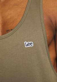 Olivgrünes Tanktop mit einem figurbetonten Design, das auf der Vorderseite ein kleines, weißes und marineblaues gesticktes "Lee"-Logo und eine glatte Textur aufweist.