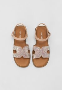 Sandales à lanières avec une bride de cheville en cuir nude, ornées de strass multicolores formant une croix sur la semelle.