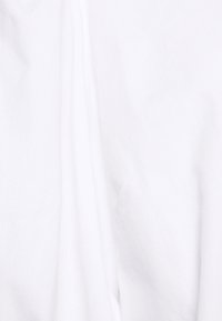 Bílá bavlněná látka s hladkou texturou a mírným splýváním, charakterizovaná jemnými záhyby a minimálním leskem.