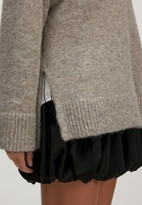 Beiger Strickpullover mit gerippten Bündchen, seitlichen Schlitzen und einer sanften Textur, kombiniert mit einem schwarzen, strukturierten, gerafften Rock.