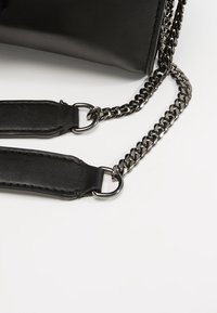 Czarna skórzana torebka na łańcuchu. Pasek posiada czarne skórzane akcenty i metalowe pierścienie, prezentując elegancki design.