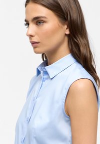 Camicia senza maniche azzurro chiaro con colletto a punta, chiusura con bottoni e una texture liscia. Il design semplice sottolinea uno stile classico.