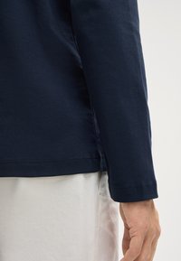 Maglietta a maniche lunghe di color navy realizzata in morbido cotone, con scollatura rotonda e orlo dritto. Presenta una texture liscia e dettagli cuciti ai polsini.