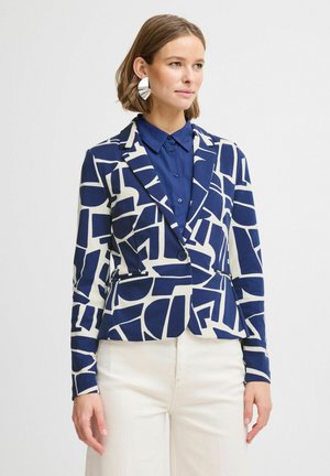 Námořnický a bílý vzorovaný blazer s upraveným střihem, klopovým límcem, dvěma předními kapsami a zapínáním na jeden knoflík, nošený přes modrou košili.