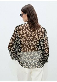 Svart blomsterblus i genomskinligt material med långa, lösa ärmar, som har ett prydnads mönster av prästkragar, en transparent textur och rundad nederkant.