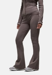 Pantalons de sport évasés en tissu côtelé marron muted, associés à des baskets de course grises. La veste a une fermeture éclair à l'avant et des poignets avec trou pour le pouce.