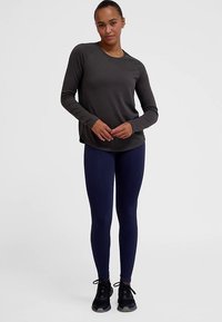Dunkelgraues Langarmshirt mit rundem Ausschnitt, kombiniert mit marineblauen Leggings. Schwarze Sportschuhe vervollständigen das Outfit. Glatte Stoffstruktur.