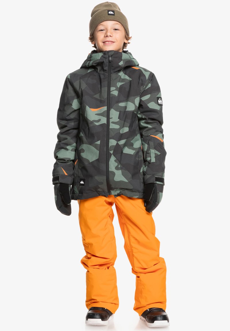 Kamouflagejacka med svarta, gröna och orange mönster; orange snöbyxor; svarta snöboots; grön mössa; handskar.