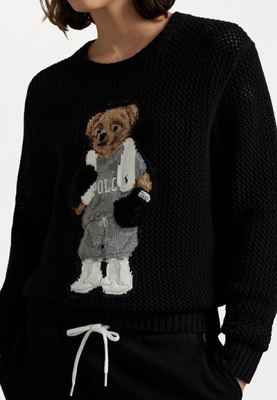Zwarte gebreide trui met een berenontwerp in grijs sportkleding. Gebreide textuur met geribde boorden en onderrand, witte trekkoord in de taille.