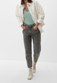 Ležérní outfit s světle zeleným žebrovaným topem bez rukávů, oversized bílou košilí, šedými džínami s vysokým pasem a béžovými teniskami na šněrování.