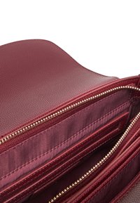 Borsa in pelle bordeaux con esterno testurizzato, chiusure con zip dorate e interno foderato in satin con diverse tasche per carte e tasche con zip.