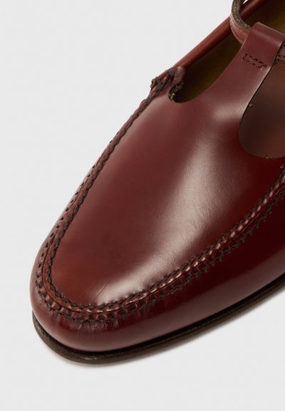 Chaussure en cuir brun avec un bout arrondi, des coutures décoratives le long des bords, et des découpes sur les côtés pour la ventilation.