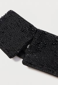 Poseta de mână din țesătură neagră, decorată cu bijuterii și mărgele negre de diferite dimensiuni, având o textură netedă și un design pliabil.