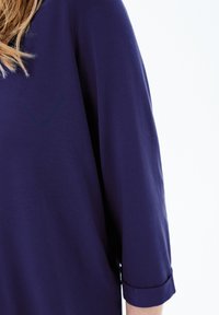 Lämpö sininen paita, jossa on kolme neljännestä hihoista, sileä tekstuuri, rento malli, jossa on käärityt hihat, suunniteltu mukavuuden ja monikäyttöisyyden vuoksi.