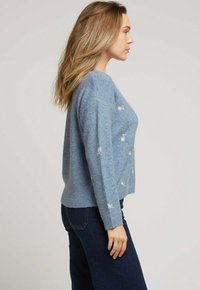 Pull en laine bleu clair avec un col rond, des épaules tombantes et des motifs floraux brodés sur le devant et les manches.