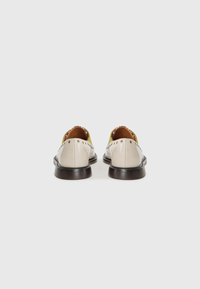 Beige leather shoes with a rounded toe, featuring gold stud accents on the heel and a dark wooden sole. Open backing reveals brown interior.