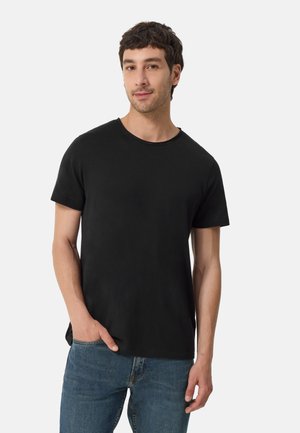 Camiseta negra de manga corta con cuello redondo, hecha de algodón suave. Se lleva con jeans de mezclilla azul, mostrando un ajuste relajado y detalles mínimos.