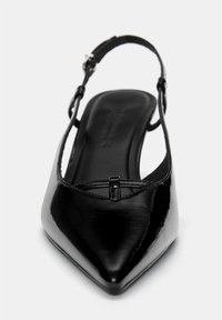 Chaussure slingback en cuir verni noir avec un bout pointu, une sangle ajustable et une silhouette élancée mettant en avant un détail décoratif en croix.