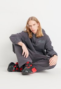 Szürke, nagyméretű kapucnis felső, rajta a "Star Wars" logóval, amelyhez illeszkedő, bő nadrágot visel. Fekete és piros, vastag talpú sportcipők, texturált részletekkel.