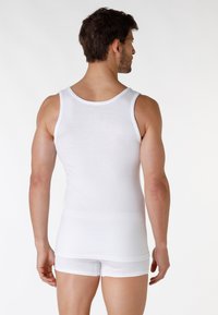 Canottiera bianca in cotone con scollatura rotonda, che presenta un design aderente e una superficie liscia, abbinata a pantaloncini bianchi.