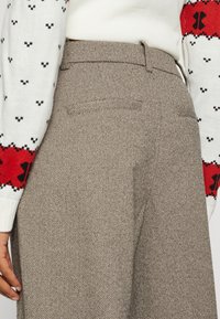 Brązowe spodnie w jodełkę o dopasowanym kroju, z tylną kieszenią i widocznym pasem. W komplecie z rękawem swetra w białe i czerwone wzory.