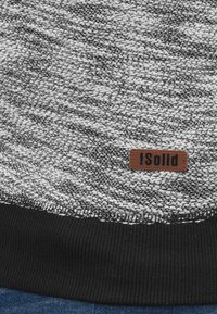 Suéter de punto en blanco y negro con un patrón texturizado. Presenta un dobladillo acanalado negro y una etiqueta marrón con el texto "iSolid."