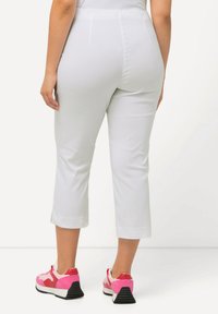 Pantalons capri blancs avec une texture lisse et des fentes latérales à l'ourlet, associés à des baskets rose et blanche avec une semelle noire.