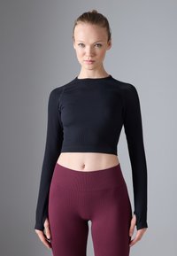 Sort langærmet crop top med ribbet tekstur, der har tommelhuller. Parret med høj-taljede bordeaux ribbede leggings.