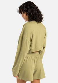 Felpa accorciata verde oliva con maniche lunghe e vestibilità ampia, abbinata a pantaloni corti coordinati. Realizzata in un tessuto morbido e testurizzato.