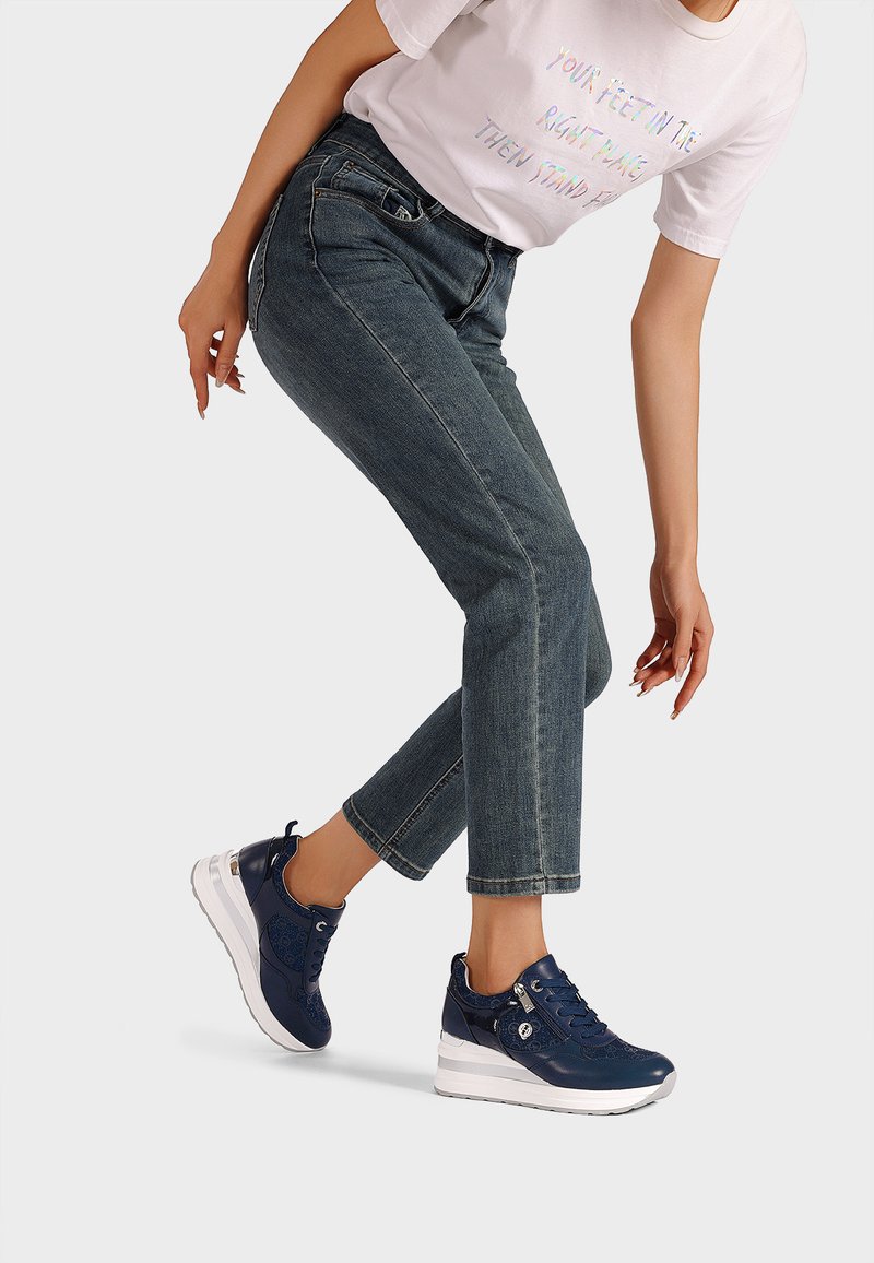 Sneakers blu navy con finitura in pelle liscia, suola platform bianca e design con lacci. Indossati con jeans in denim azzurro.