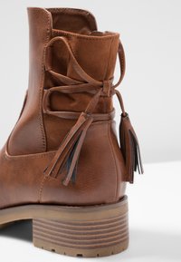 Botte chelsea en cuir marron avec une surface texturée, ornée d'un lacet avec des glands et d'un talon empilé avec des rainures horizontales.