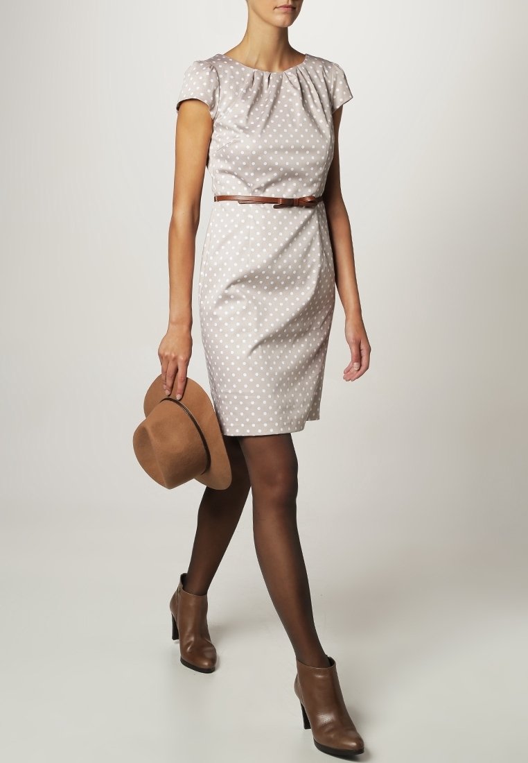 Abito a pois marrone chiaro con maniche corte, cintura in vita, abbinato a un cappello marrone e stivaletti alla caviglia. Tessuto morbido e design aderente.