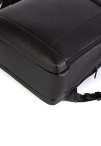 Mustan nahkarepun teksturoitu pinta, suorakulmainen muoto, vetoketjukiinnitys ja säädettävät hihnat, joissa on minimaalista metalliosaa ja puhtaat linjat.