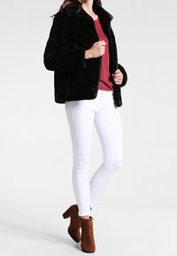 Svart fuskpälsjacka med krage, kombinerad med en vinröd topp, vita smala jeans och bruna ankelsboots. Enkla, moderna designelement.