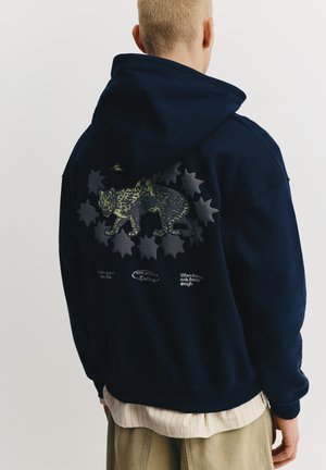 Marineblå hættetrøje med en stor grafik af en leopard omgivet af stjerneformede figurer på ryggen. Har ribbede manchetter og kant.