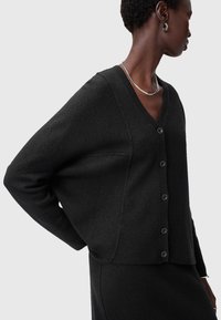 Svart stickad cardigan med V-hals, framknappar, vida ärmar och ribbad nederkant. Slät textur och avslappnad passform.