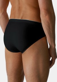 Slip da nuoto neri con una superficie liscia, taglio a vita bassa e una sottile cintura a contrasto, che mettono in mostra un design minimalista e una forma aderente.