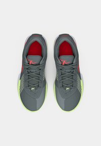 Grijze sportschoenen met rode accenten, textuurstof, mesh-panelen en een felgroene zool. Beschikt over een gevoerde tong en een klassieke vetersluiting.