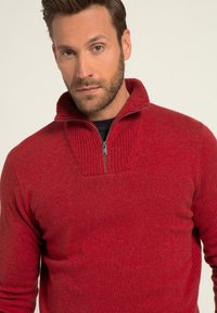 Sweatshirt zippé rouge avec un col haut à côtes et un tricot texturé. Présente un panneau en tricot plat au niveau de la poitrine et des manches ajustées.
