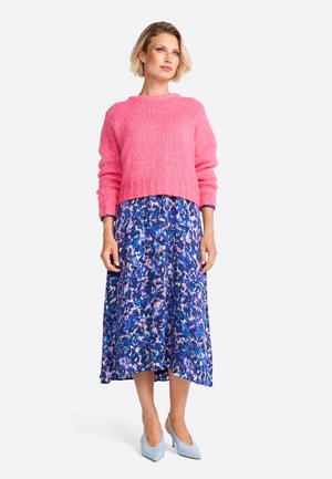 Rosa Strickpullover mit geripptem Muster, kombiniert mit einem blauen Midikleid mit Blumendruck. Hellblaue High Heels runden das Outfit ab.