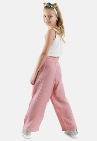 Roze, geribde wijde broek met een elastische tailleband, gedragen met een witte mouwloze top en grijze sneakers.