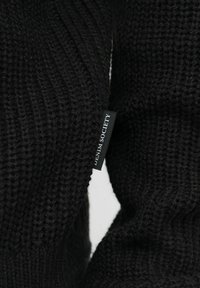 Suéter negro de punto con textura de canalé. Presenta una pequeña etiqueta que dice “DENIM SOCIETY” unida a la costura lateral.