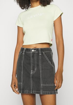 Nainen, joka pukeutunut vaaleankeltaiseen lyhyeen Levi'sin t-paitaan ja korkeavyötäröiseen mustaan farkkuhameeseen, jossa on valkoiset ompelut.