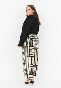 Donna in top nero a maniche lunghe e pantaloni ampi a vita alta con motivo geometrico bianco e nero, che indossa tacchi a slingback neri.